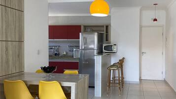 A modern kitchen with a central island, yellow chairs, a red cabinet, and a yellow pendant light.
