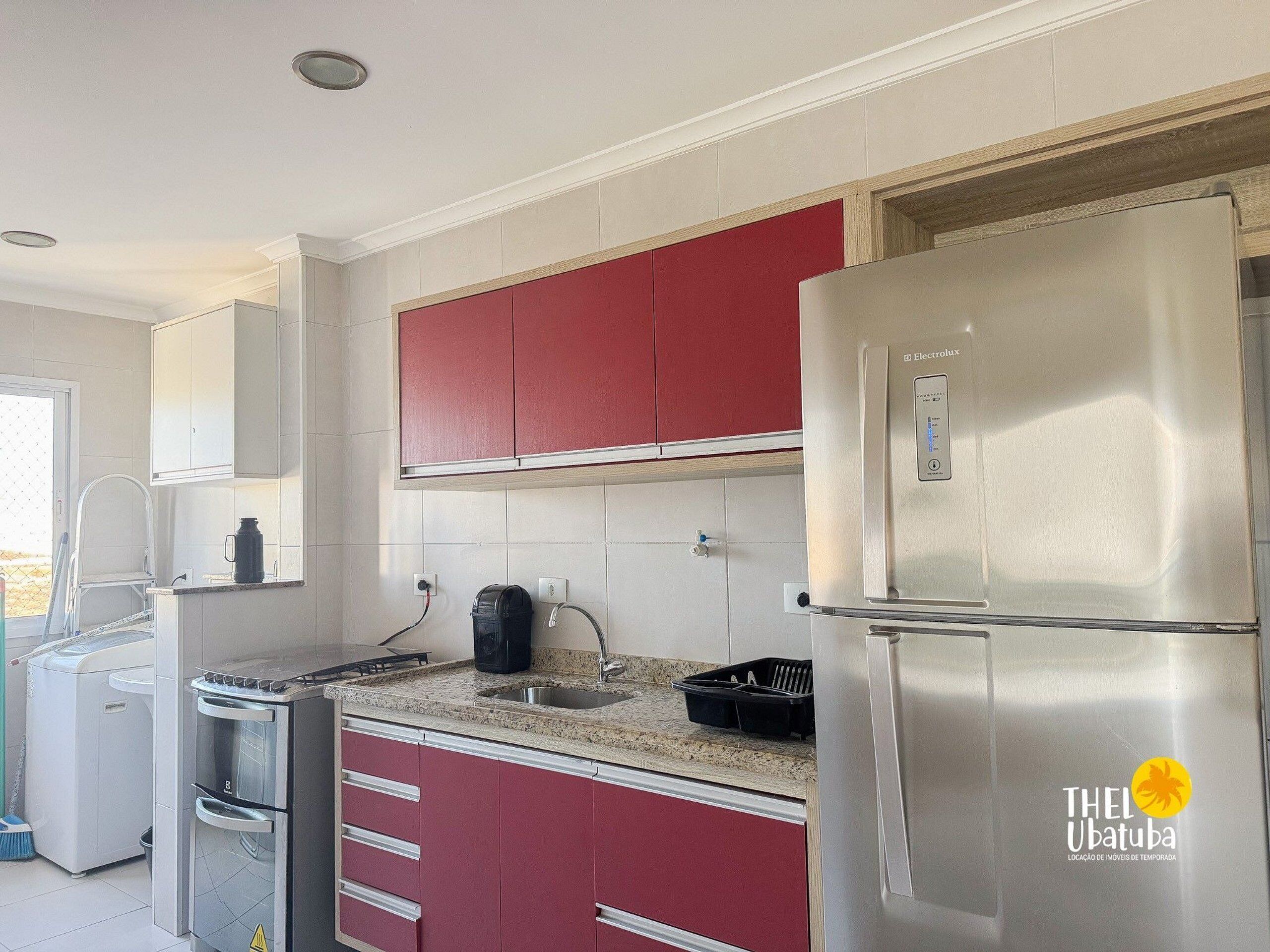 A modern kitchen with stainless steel appliances, red cabinets, and a granite countertop.