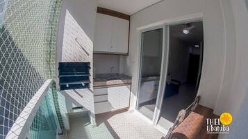 Uma pequena varanda com área de cozinha, incluindo pia e armários, e uma porta de vidro deslizante que dá para um espaço interno.