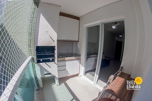 Uma pequena varanda com área de cozinha, incluindo pia e armários, e uma porta de vidro deslizante que dá para um espaço interno.