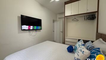 Quarto com cama, televisão na parede, guarda-roupa e ventoinha no teto.