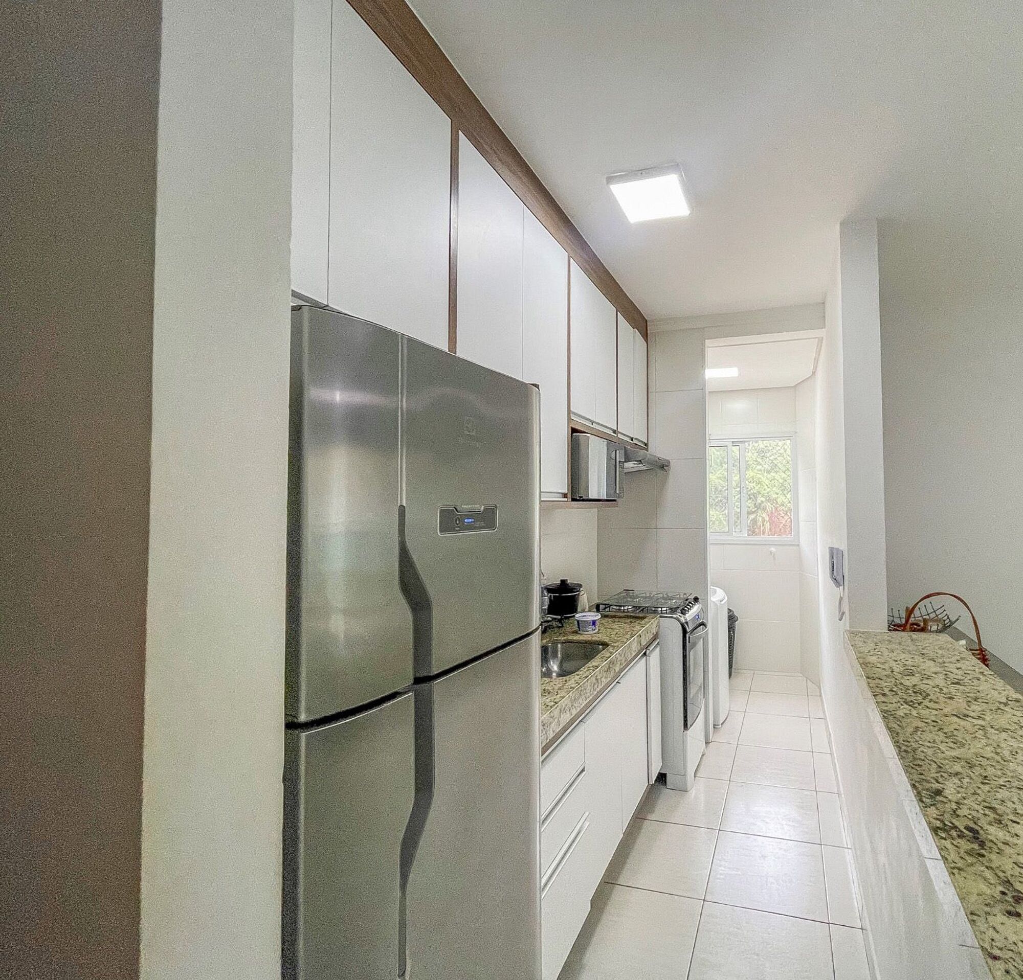 Uma cozinha moderna com eletrodomésticos de aço inoxidável, armários brancos e piso ladrilhado.