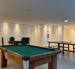 A billiards room with a pool table, a ping pong table, and a seating area with chairs.