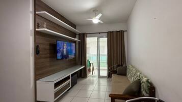 Uma sala de estar moderna com televisão de tela plana, prateleiras de madeira, sofá e um espaço para refeições.