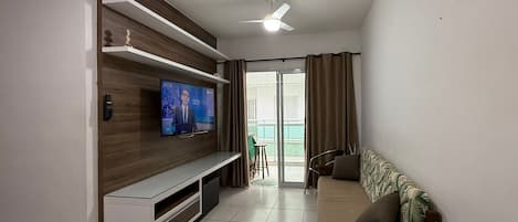 Una sala de estar moderna con televisor de pantalla plana, estanterías de madera, un sofá y una zona de comedor.