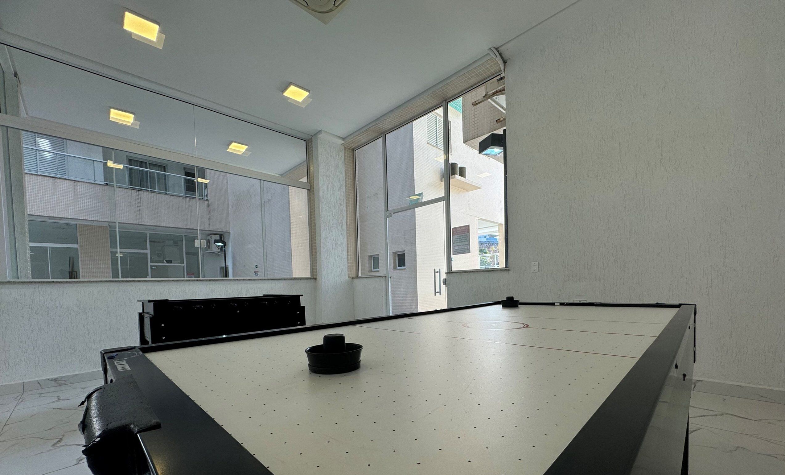 A conference room with a large table, a black chair, and a window with blinds.