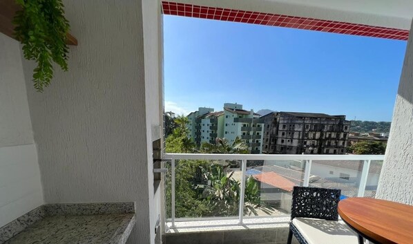A balcony with a view of buildings, a wooden table, and a chair. - Thel Ubatuba - Apto 34/A, Ibiza - Praia Grande (Ubatuba)