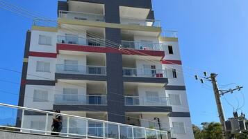 Edifício residencial com vários andares, varandas, uma pessoa no andar térreo e infraestrutura elétrica visível.
