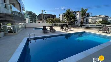 Piscina no terraço com espreguiçadeiras e vista para edifícios próximos.