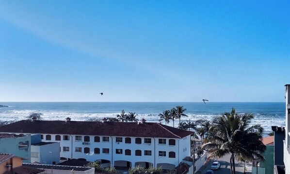Een gebouw aan de kust met veel ramen, uitzicht op zee en palmbomen.