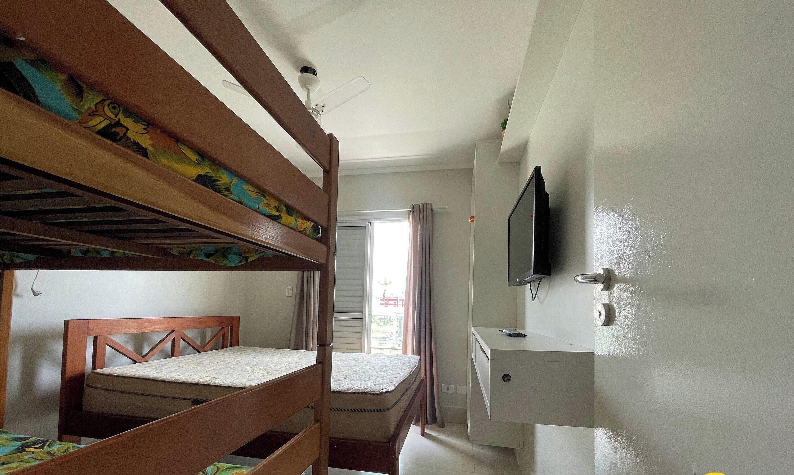A room with bunk beds, a desk, a chair, a television, and a window with curtains.