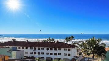 Um edifício costeiro com várias janelas, vista clara do oceano e palmeiras.
