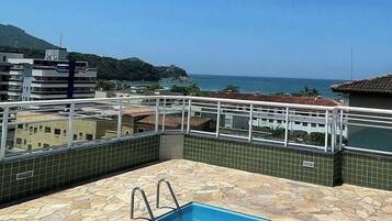Piscina no terraço com vista clara para o mar e montanhas ao fundo.