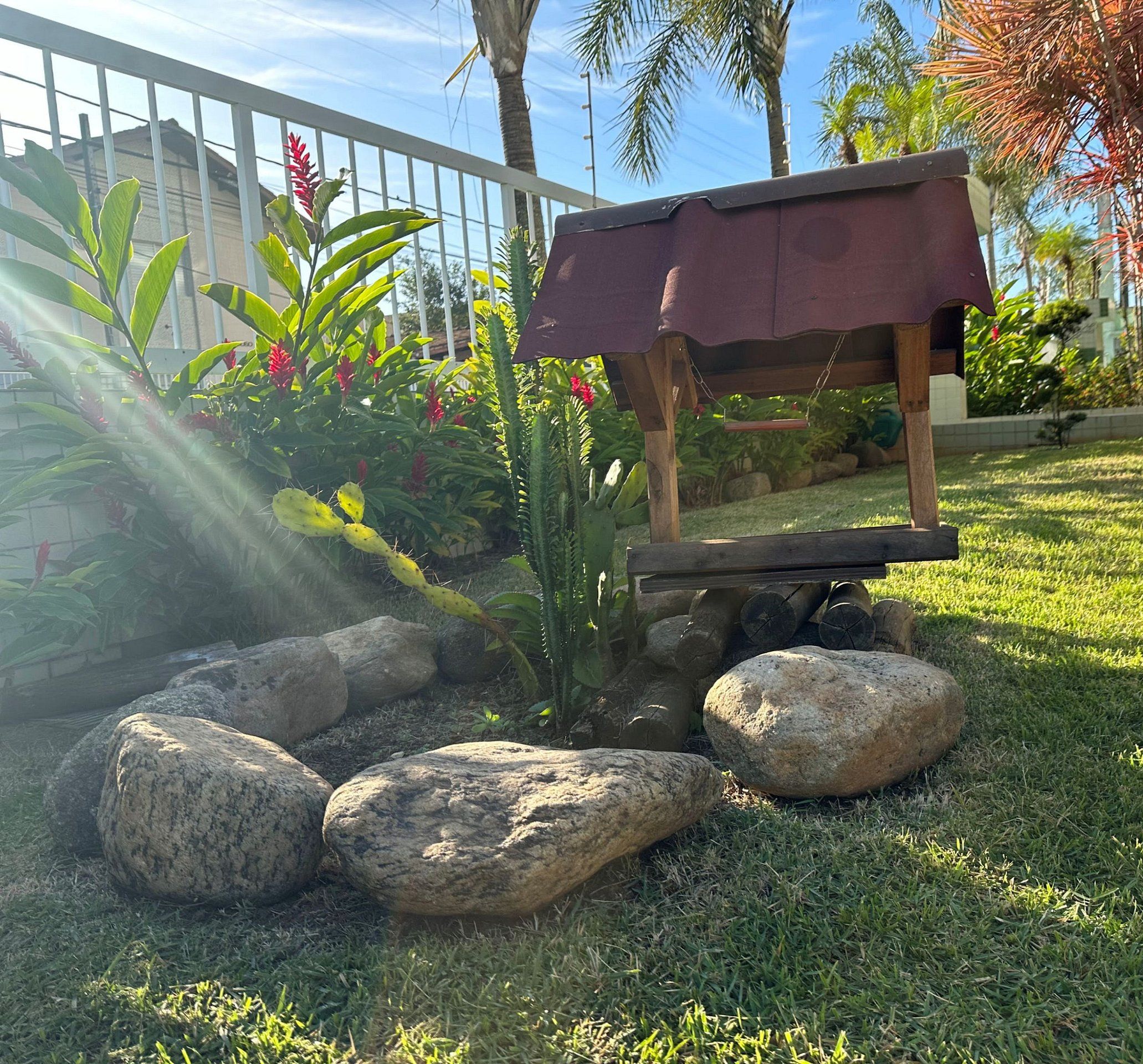 Um jardim com um banco de madeira, pedras e plantas tropicais.