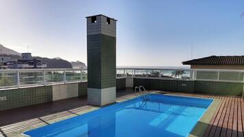 A rooftop swimming pool with a view of the ocean and a cityscape in the background.