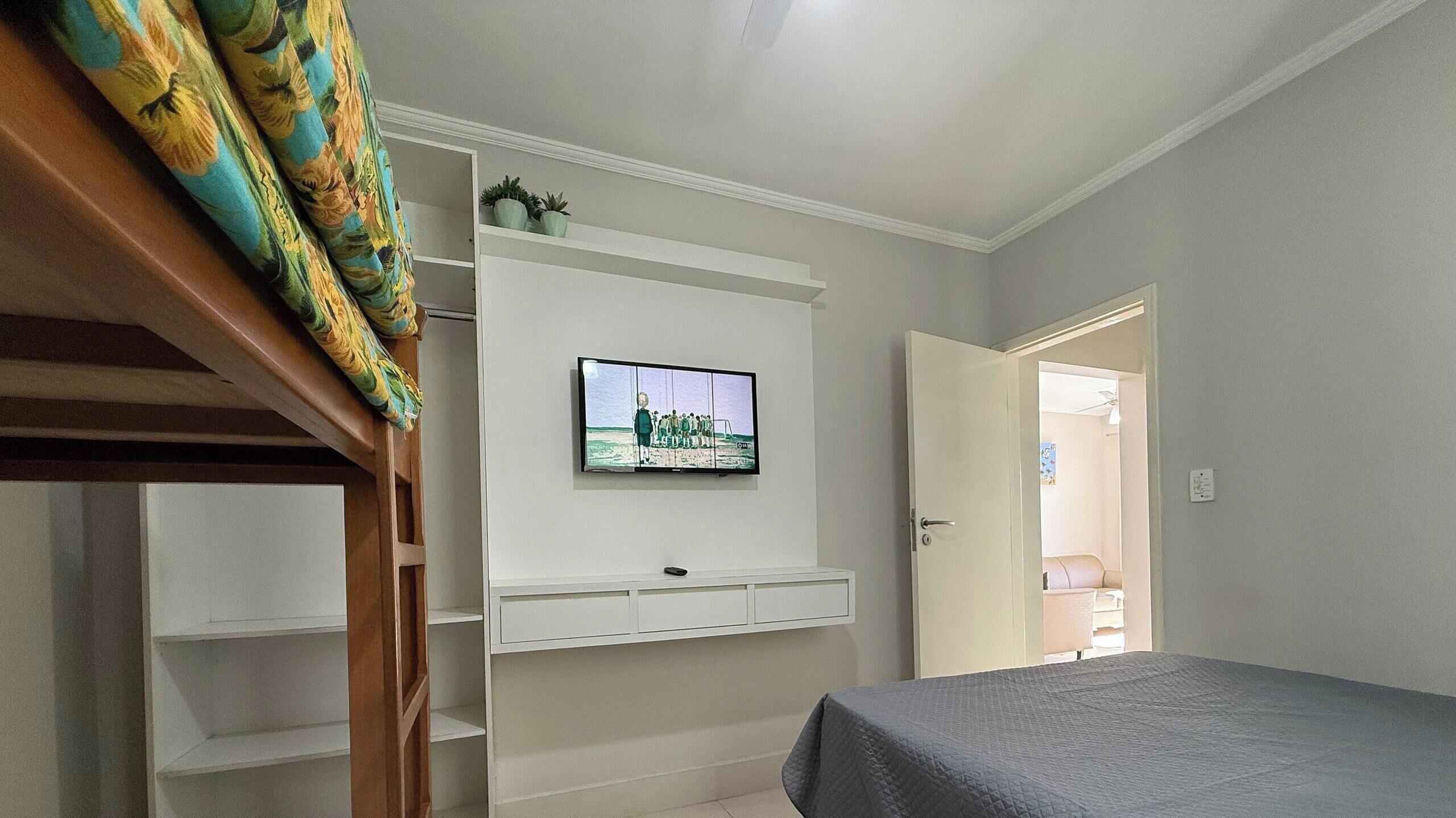 A bedroom with a bed, a TV mounted on a wall, and a door leading to another room.