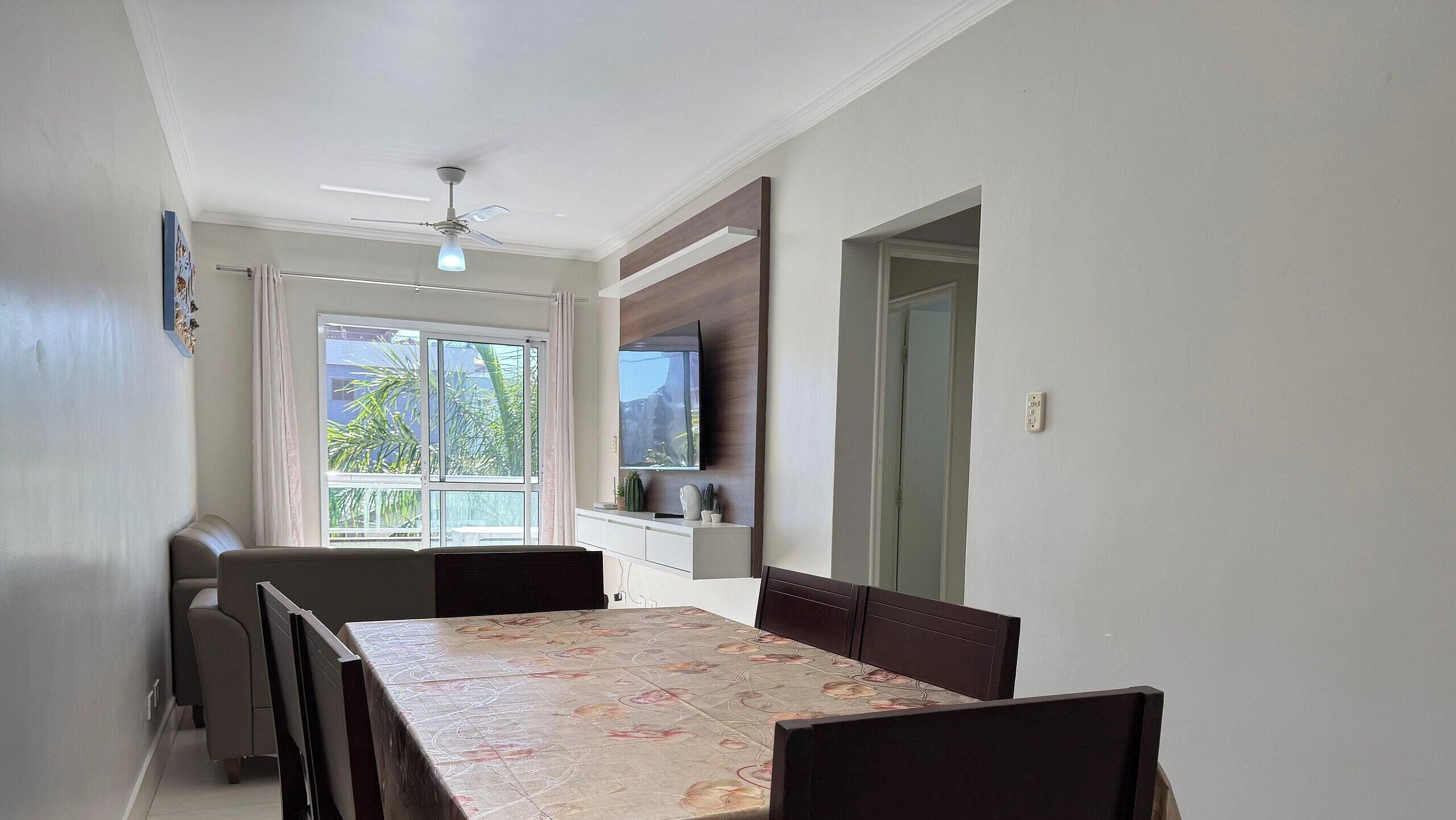A dining area with a table, chairs, a ceiling fan, and a TV mounted on the wall.