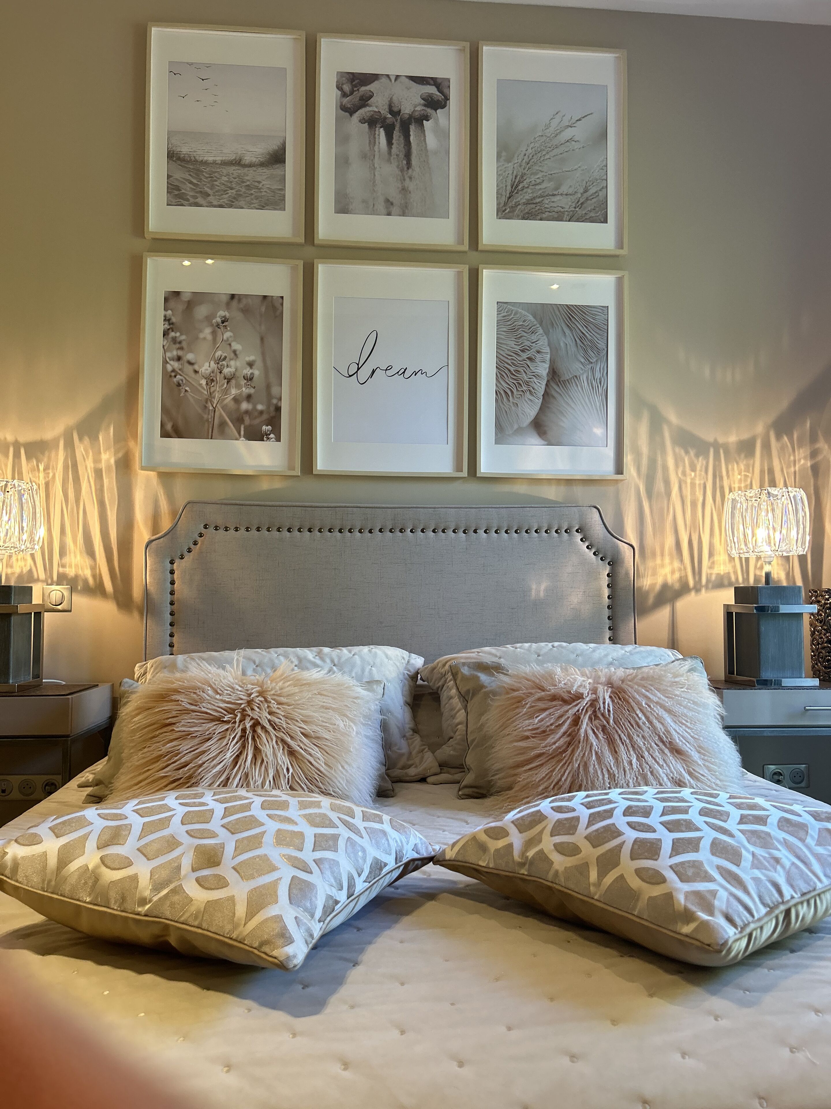 Ein Schlafzimmer mit einer gebügelten Kopfteil, zwei Zierkissen, einem gerahmten Kunstwerk über dem Bett und Nachttischlampen.