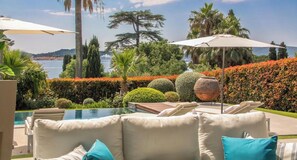 A poolside area with lounge chairs and umbrellas, a view of the sea, and well-maintained landscaping.
