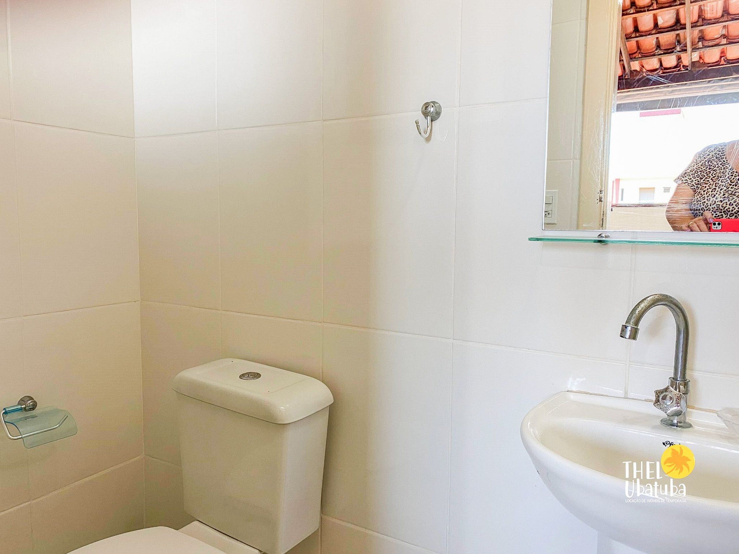 A bathroom with white tiles, a toilet, a glass shelf, and a sink with a faucet.