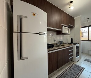 A modern kitchen with a white refrigerator, dark wooden cabinets, a microwave, and a gas stove. - Thel Ubatuba - Praia Grande - Saint Patrick - Apto 406 (Ubatuba)