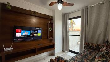 Una sala de estar moderna con un televisor de pantalla plana, mueble de madera para entretenimiento, ventilador de techo y vista al exterior desde un balcón.