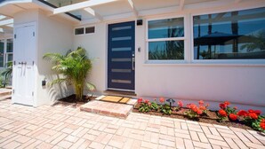 A modern house with a white exterior, a dark blue door, and a small garden with red flowers. - La Jolla Windansea Luxury Cottage (San Diego)