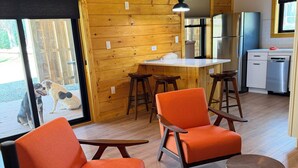 A modern interior with wooden walls, a kitchen area, and two orange chairs with wooden legs. - Charming 1BR Barn Retreat – Close to Hospitals, Parks & Town in  Mooresville (Mooresville)