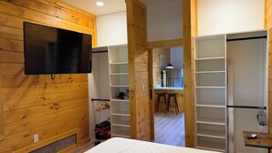 A room with wooden paneling, a bed, a TV, a kitchen area, and a bathroom with a shower. - Charming 1BR Barn Retreat – Close to Hospitals, Parks & Town in  Mooresville (Mooresville)