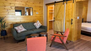 A room with a wooden wall, a sofa, a chair, a small table, and a sliding door. - Charming 1BR Barn Retreat – Close to Hospitals, Parks & Town in  Mooresville (Mooresville)