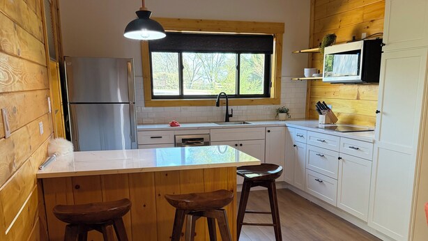 A kitchen with wooden walls, a stainless steel refrigerator, a window, and a wooden island with stools. - Charming 1BR Barn Retreat – Close to Hospitals, Parks & Town in  Mooresville (Mooresville)