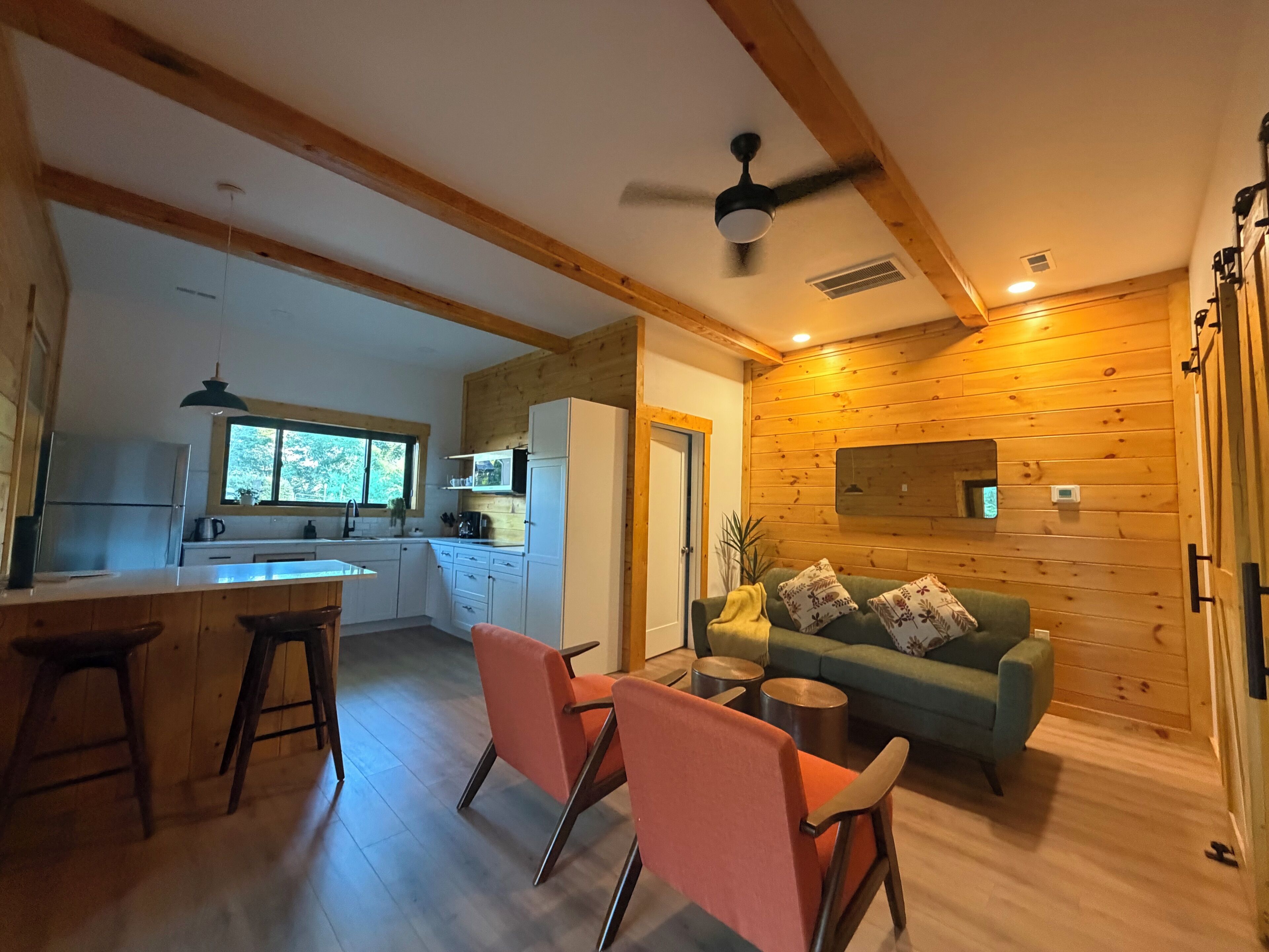 A modern kitchen with wooden beams, a dining area with a green sofa, and a ceiling fan.
