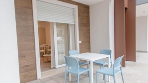 A modern dining area with a white table and four light blue chairs, a sliding glass door, and a view into a room with a sofa and a coffee table.