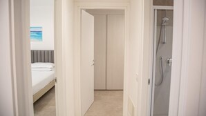 A hotel room with a bed, a shower, and a door leading to another room.