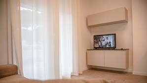 A modern living room with a television on a white cabinet, sheer curtains, and a beige sofa.