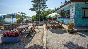 An outdoor seating area with wooden tables and benches, umbrellas, and a building with a blue and white pattern.