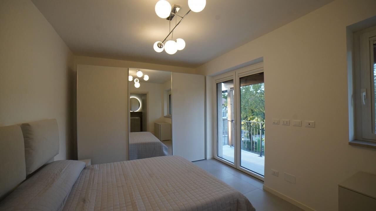 A modern bedroom with a large bed, a walk-in closet, and a sliding glass door to a balcony.