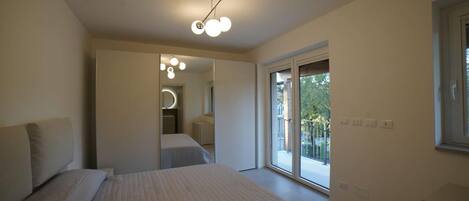 A modern bedroom with a large bed, a walk-in closet, and a sliding glass door to a balcony.