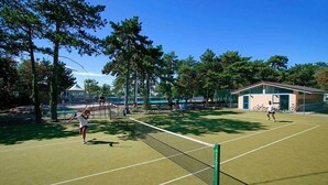 A tennis court with players, trees, and a building in the background.