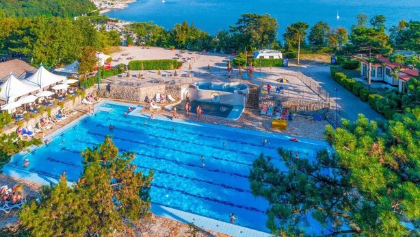A large outdoor swimming pool with multiple lanes, surrounded by lounge areas and a scenic view of the sea.