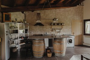 Una cocina con lavadora, barriles de madera, un taburete de bar y una lámpara colgante.