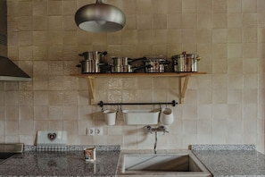 A kitchen with a granite countertop, a sink, a hanging pot rack, and a pendant light.