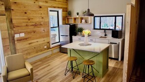 A modern kitchen with wooden walls, a green island, bar stools, a chair, and a view of the forest through the window. - Serenity Barn, cozy barn-dominium with a great locatoin (Mooresville)