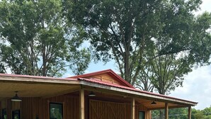 A wooden cabin with a covered porch, a lawn, and trees in the background. - Serenity Barn, cozy barn-dominium with a great locatoin (Mooresville)