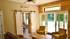 A room with a wooden ceiling, a ceiling fan, a sofa, two armchairs, a coffee table, and a sliding glass door leading to an outdoor area. - Serenity Barn, cozy barn-dominium with a great locatoin (Mooresville)
