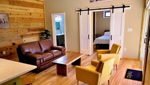 A modern living room with a brown leather sofa, yellow armchairs, a wooden coffee table, and a sliding door leading to a bedroom. - Serenity Barn, cozy barn-dominium with a great locatoin (Mooresville)