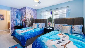 A bedroom with two beds, each with a snowman-themed bedspread, a large mural of animated characters on the wall, and a window with blinds.