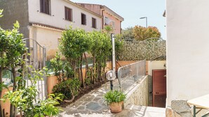 A narrow stone pathway flanked by potted plants and a metal railing, leading to a building with a beige facade and windows with shutters. - Petali di Rosa – A Due Passi dalla Spiaggia (Loiri)