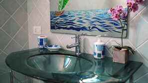 A bathroom with a glass sink, a faucet, a soap dispenser, and a decorative mirror with a wave pattern.