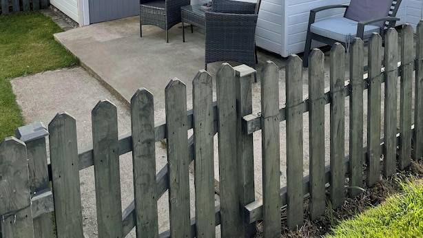 Une maison mobile blanche avec une porte grise, deux chaises en osier et un petit espace patio.